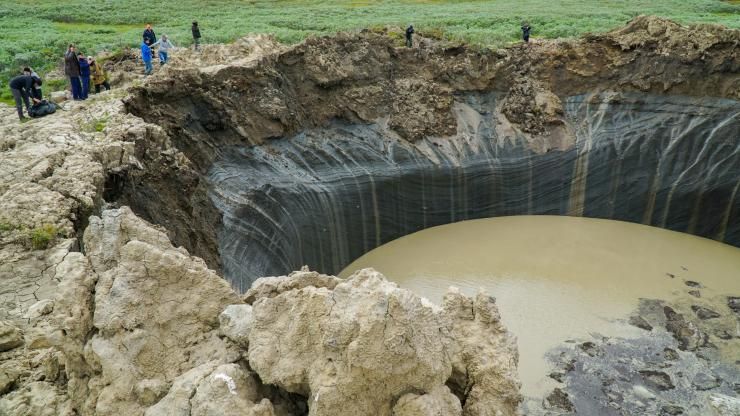 En Sibérie, des personnes se trouvent juste au bord d'un trou d'origine inconnue, d'une dizaine de mètres de diamètre, très profond et contenant de l'eau.