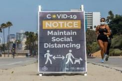 A Long Beach en Californie une joggeuse passe devant un panneau appelant à maintenir les distances sociales, le 14 juillet 2020 © AFP Apu GOMES