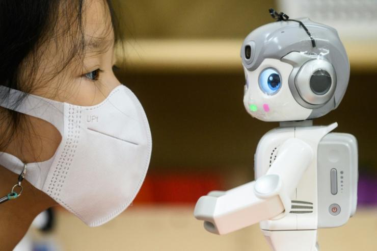 Une élève d'une école maternelle regarde le robot "Alpha Mini", qui peut cligner des yeux, danser, chanter, le 23 novembre 2021 à Séoul, en Corée du Sud © AFP Anthony WALLACE